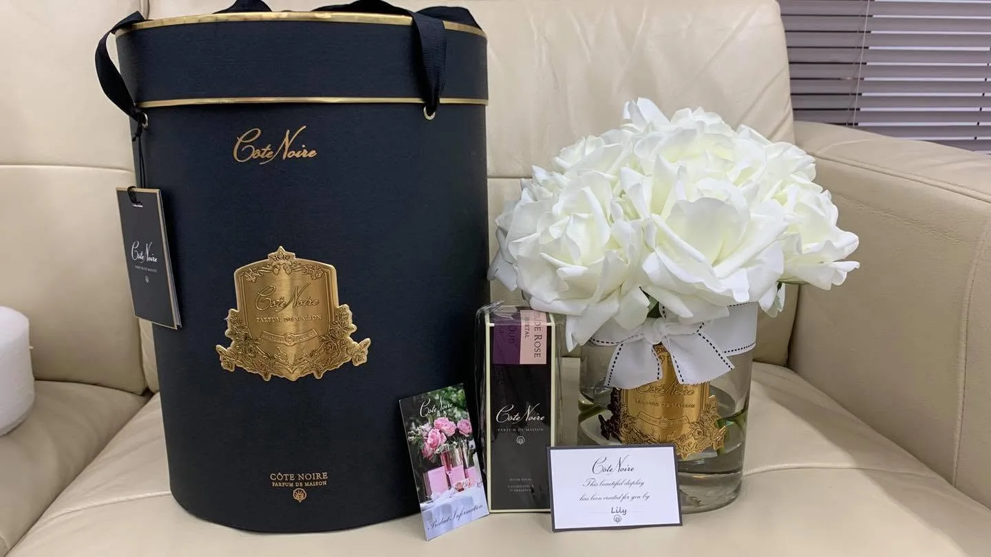 Côte Noire large navy hatbox with white perfumed roses and room spray, 'created for you by Lily' card on a cream sofa