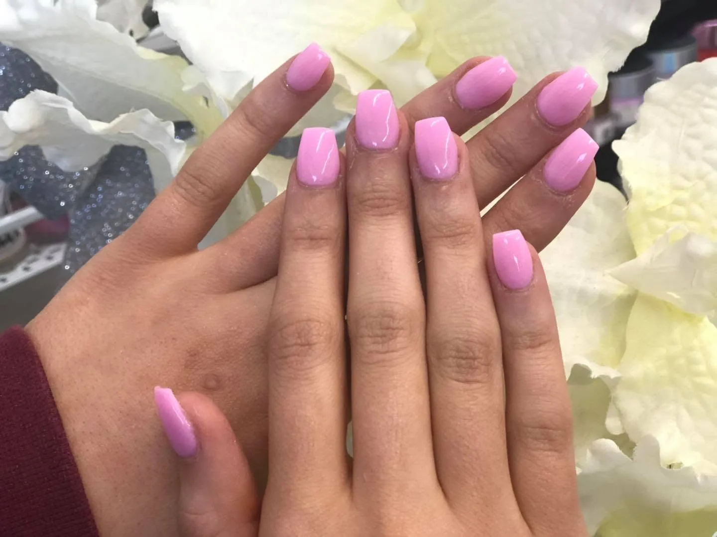Pale-pink square gel nails with white flowers and polish bottles in the background