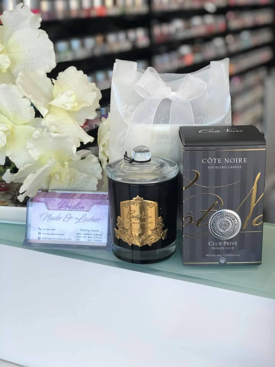 Côte Noire black-and-gold candle and boxed candle arranged on the salon counter with white flowers