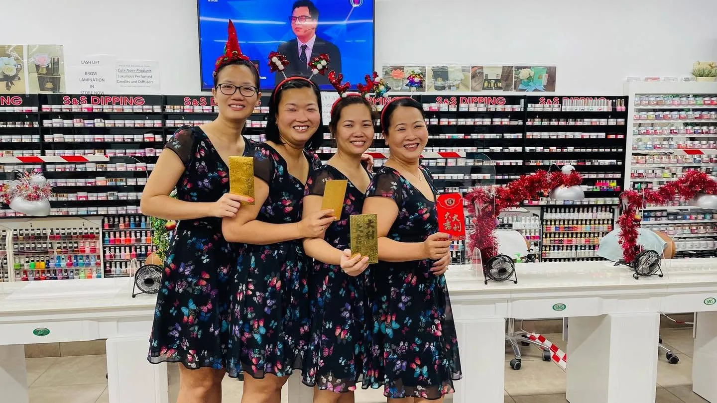 Team members in matching butterfly-print dresses in the salon, in front of the Lash Lift and Brow Lamination signage and the S&S Dipping wall