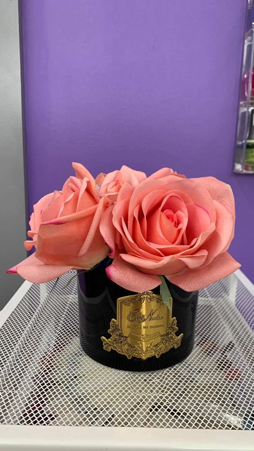 Côte Noire coral perfumed roses in a black vase on a white stand against the salon's lilac feature wall