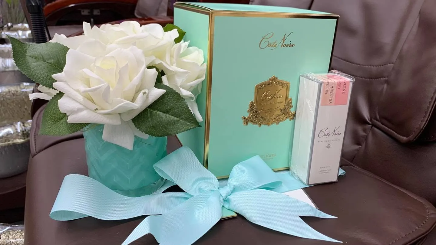 Côte Noire black gift box with room spray and pale-pink perfumed rose on a cream sofa