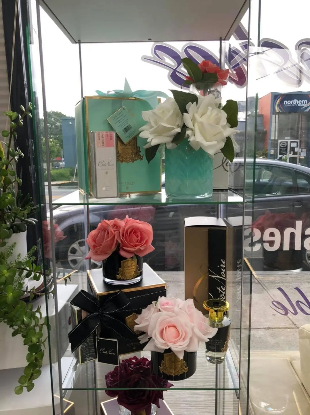 Glass cabinet of Côte Noire perfumed roses and boxes, potted plant and shopfront window with 'Preston Nails & Lashes' signage