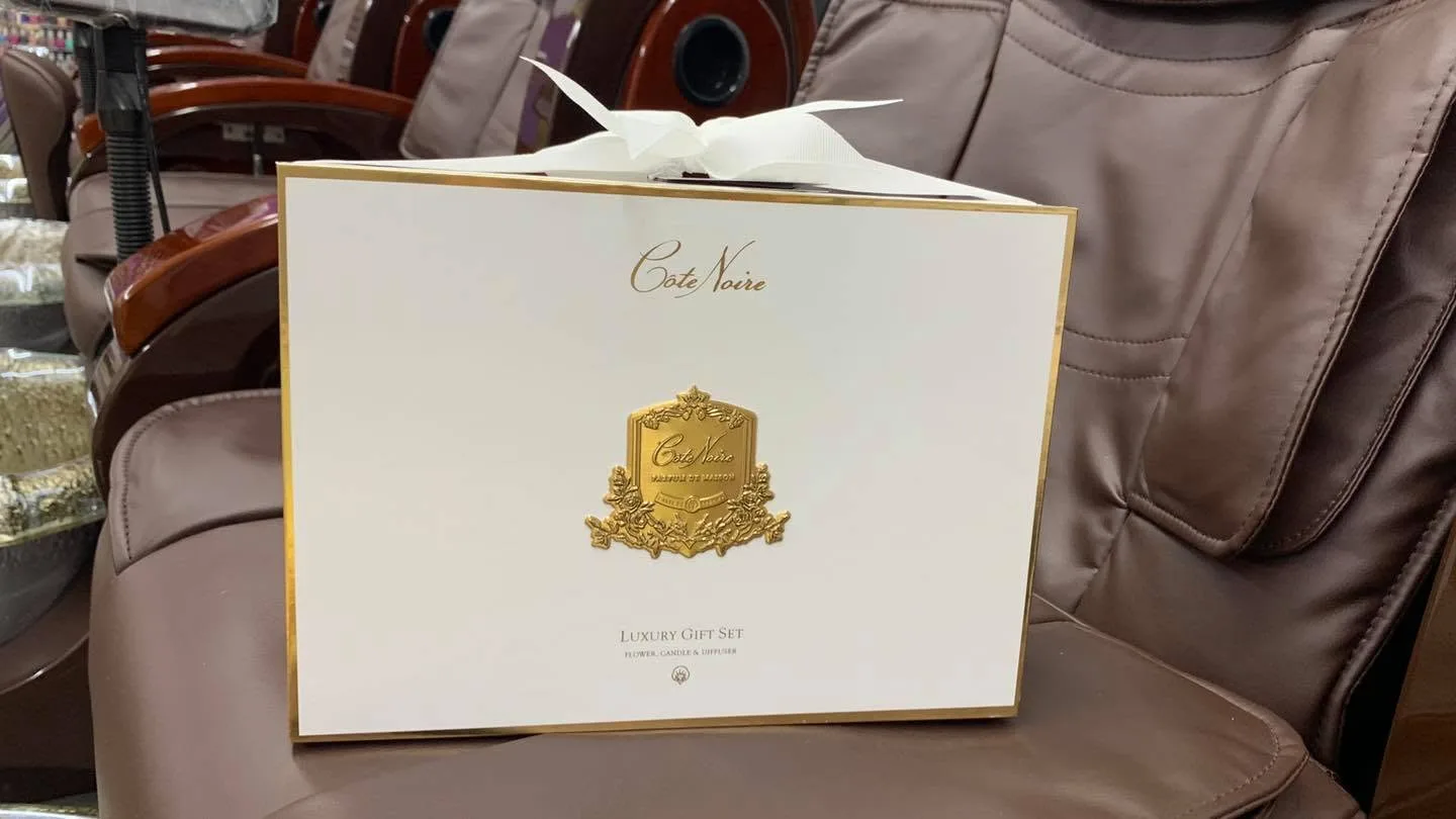 Côte Noire white-and-gold 'Luxury Gift Set — Flower, Candle & Diffuser' box with bow on a brown pedicure chair